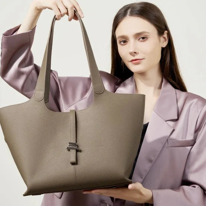 Woman in purple satin blazer holding large taupe leather tote bag against plain background
