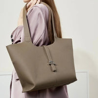 Taupe leather tote bag with silver clasp, worn on shoulder, minimalist style