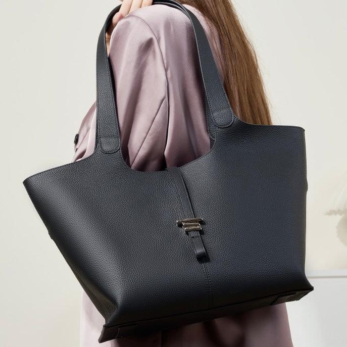 Woman in mauve blouse carrying a large black leather tote bag with silver buckle detail