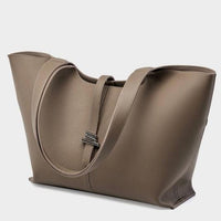 Taupe leather tote bag with double handles and minimalist silver clasp on gray background