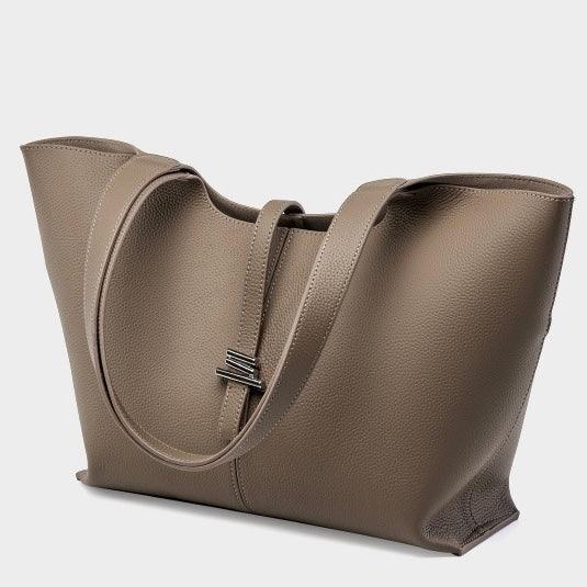 Taupe leather tote bag with double handles and minimalist silver clasp on gray background