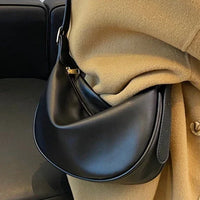 Black leather crescent shoulder bag on beige coat, modern minimalist fashion accessory