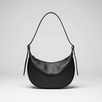 Black leather shoulder bag with curved shape on cream fabric, hand holding strap