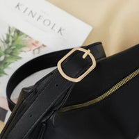 Black leather bag with gold buckle and zipper on beige surface, Kinfolk magazine in background