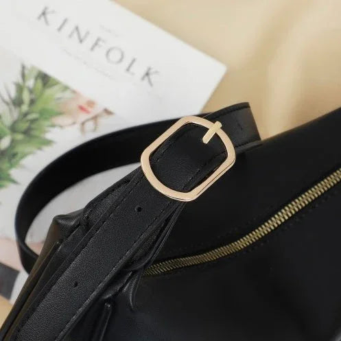 Black leather bag with gold buckle and zipper on beige surface, Kinfolk magazine in background