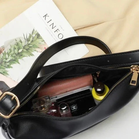 Black leather handbag open with wallet, sunglasses, perfume, and magazine on beige fabric