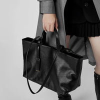 Woman in gray coat holding black leather tote bag, pleated skirt and knee-high boots