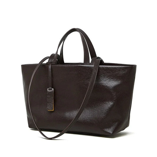 Dark brown leather tote bag with dual handles and shoulder strap on white background
