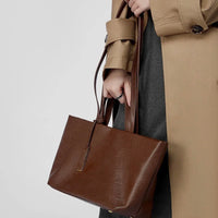 Woman in beige trench coat holding brown leather tote bag
