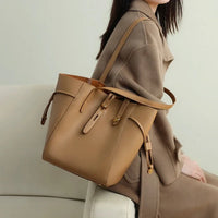 Woman in a beige coat holding a tan leather bucket bag on a light sofa