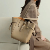 Beige leather tote bag on woman in tan coat sitting on a modern sofa
