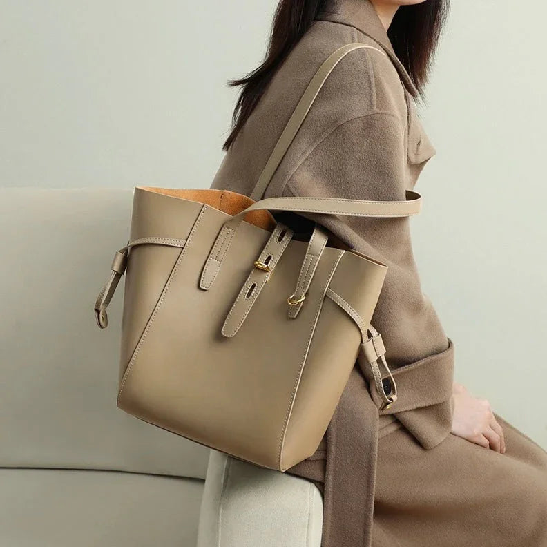 Beige leather tote bag on woman in tan coat sitting on a modern sofa