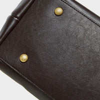 Close-up of brown leather bag bottom with gold metal feet on white background