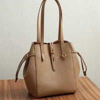 Beige leather tote bag with gold hardware on a wooden table, minimalist style