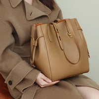 Woman in a brown coat holding a large tan leather tote bag with gold hardware