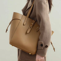 Woman wearing beige coat carrying large tan leather tote bag
