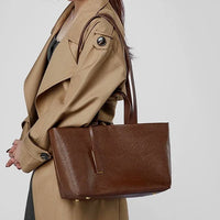 Woman in beige trench coat carrying large brown leather tote bag