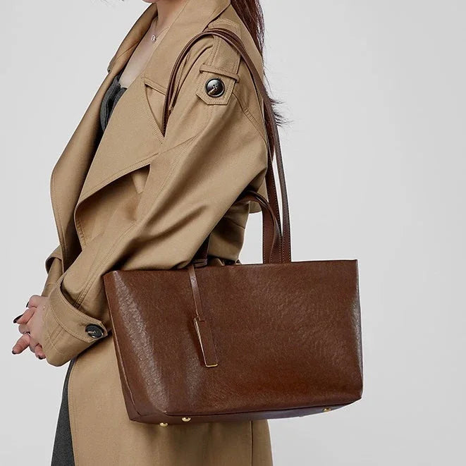 Woman in beige trench coat carrying large brown leather tote bag