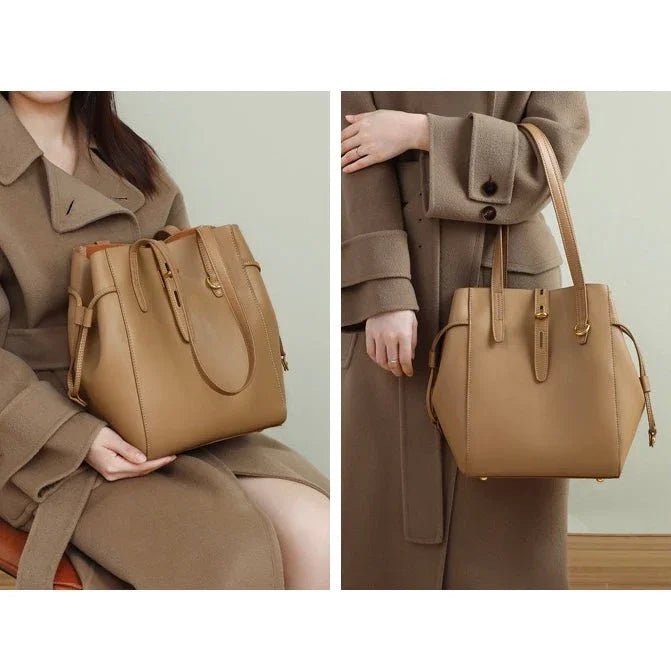 Tan leather tote bag with top handles, modeled with a beige wool coat indoors