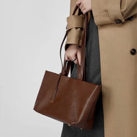 Woman in a beige trench coat holding a brown leather tote bag