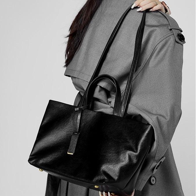 Woman in gray trench coat holding a large black leather tote bag