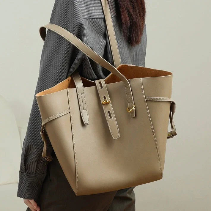 Beige leather tote bag with gold hardware on shoulder, worn by person in gray shirt