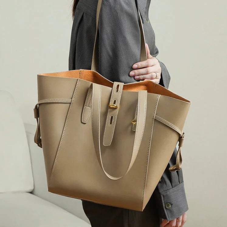 Woman holding a large beige leather tote bag with gold hardware