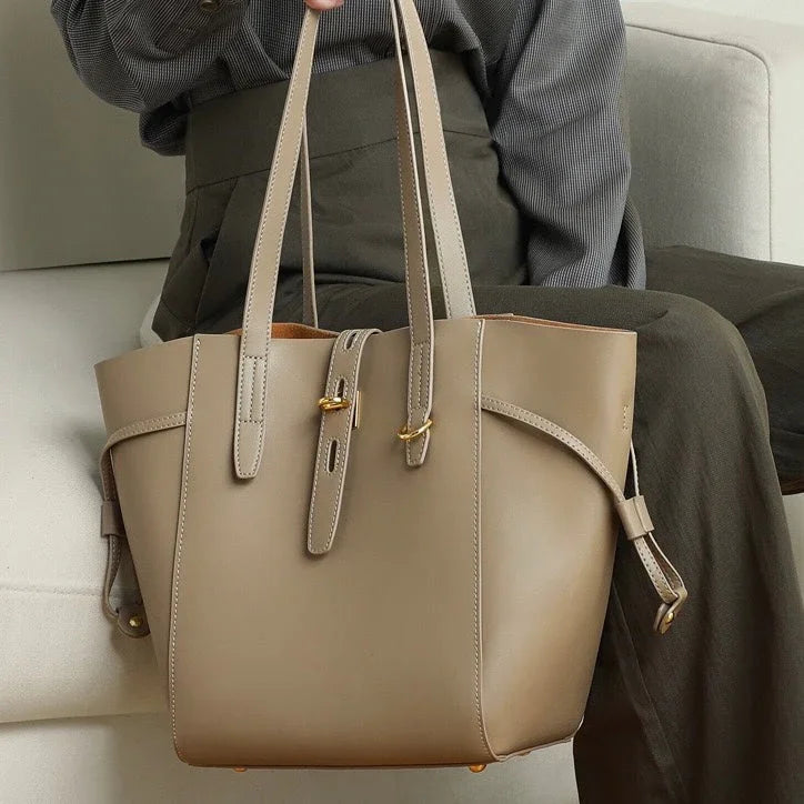Taupe leather tote bag with gold hardware on woman's lap, minimalist fashion accessory