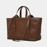 Brown leather tote bag with top handles and shoulder strap on a white background