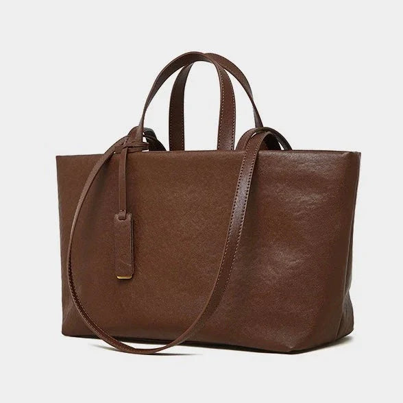 Brown leather tote bag with top handles and shoulder strap on a white background