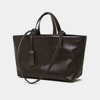 Black leather tote bag with top handles and shoulder strap on a white background