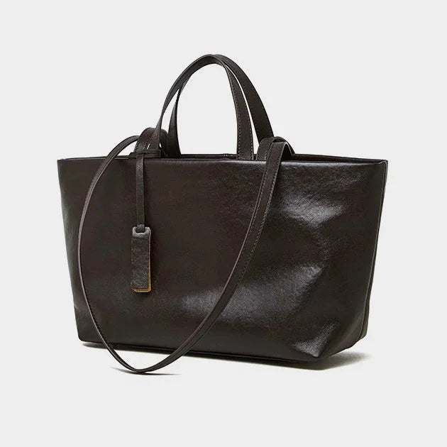 Black leather tote bag with top handles and shoulder strap on a white background