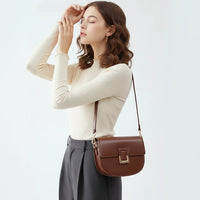 Woman wearing cream top and black pants with brown leather shoulder bag on white background
