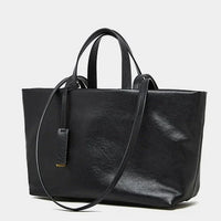 Black leather tote bag with shoulder strap and top handles on white background