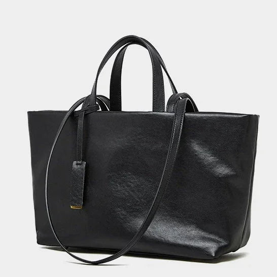 Black leather tote bag with shoulder strap and top handles on white background