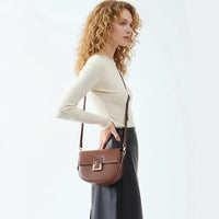 Woman wearing a beige top and black pants with a brown leather crossbody bag