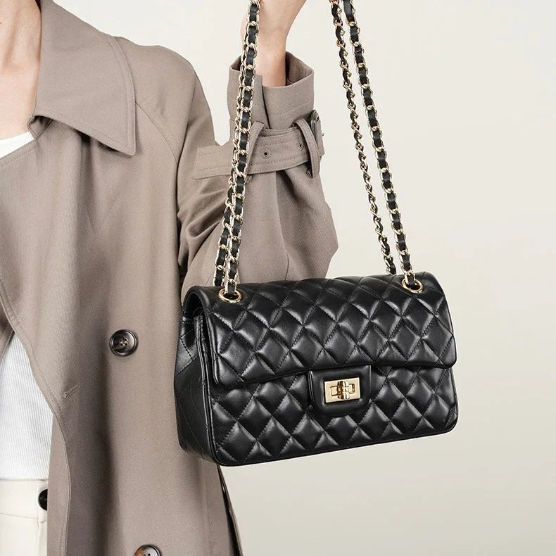 Woman in beige trench coat holding black quilted leather shoulder bag with gold chain strap