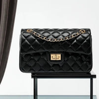 Black quilted leather handbag with gold chain strap and clasp on glass display
