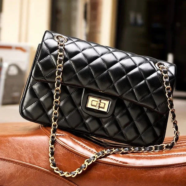Black quilted leather handbag with gold chain strap and clasp on a brown leather surface