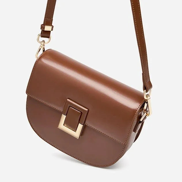 Brown leather crossbody bag with gold buckle and adjustable strap on white background