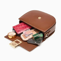 Open brown leather crossbody bag with cosmetics, wallet, phone, and makeup items inside