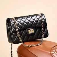 Black quilted leather shoulder bag with gold chain strap on brown leather surface