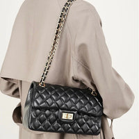 Quilted black leather shoulder bag with gold chain strap on beige coat