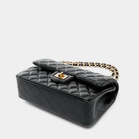 Black quilted leather handbag with gold chain strap and turn-lock clasp on white background