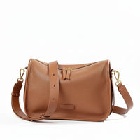 Tan leather crossbody bag with gold hardware and adjustable strap on white background