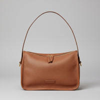 Brown leather shoulder bag with gold zipper on woven mat and wood background