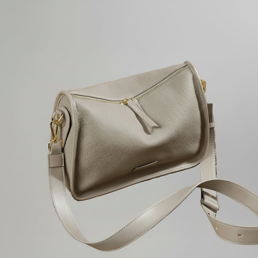 Taupe leather shoulder bag with gold hardware on woven surface, vintage clock in background