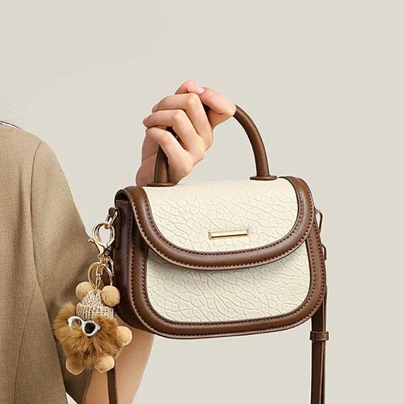Woman holding small cream and brown leather handbag with teddy bear keychain