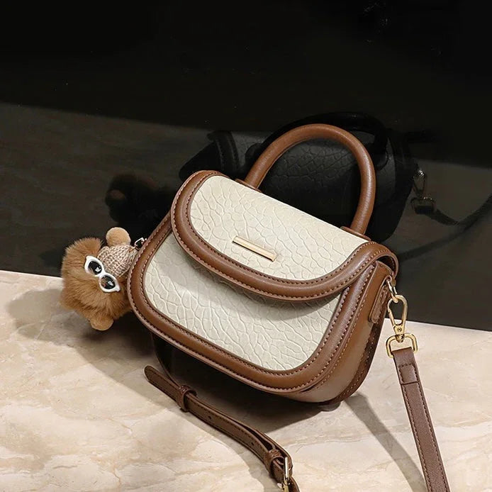 Small beige and brown crossbody handbag with textured leather and cute plush owl keychain.