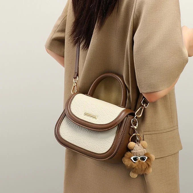Woman wearing tan dress with brown and white leather crossbody purse and bear keychain